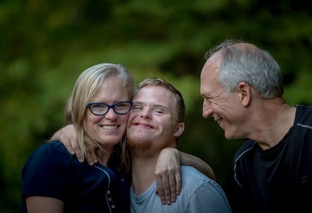 A woman embracing a boy and a man standing beside them and they're all smiling